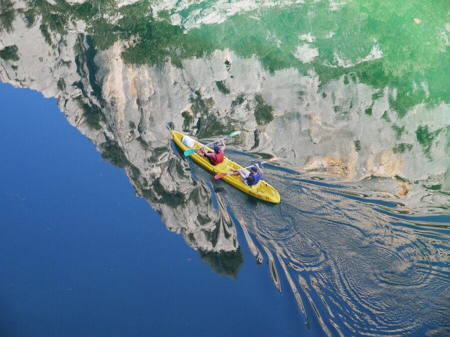Two kayakers paddling through turquoise water in the Verdon canyon seen from above