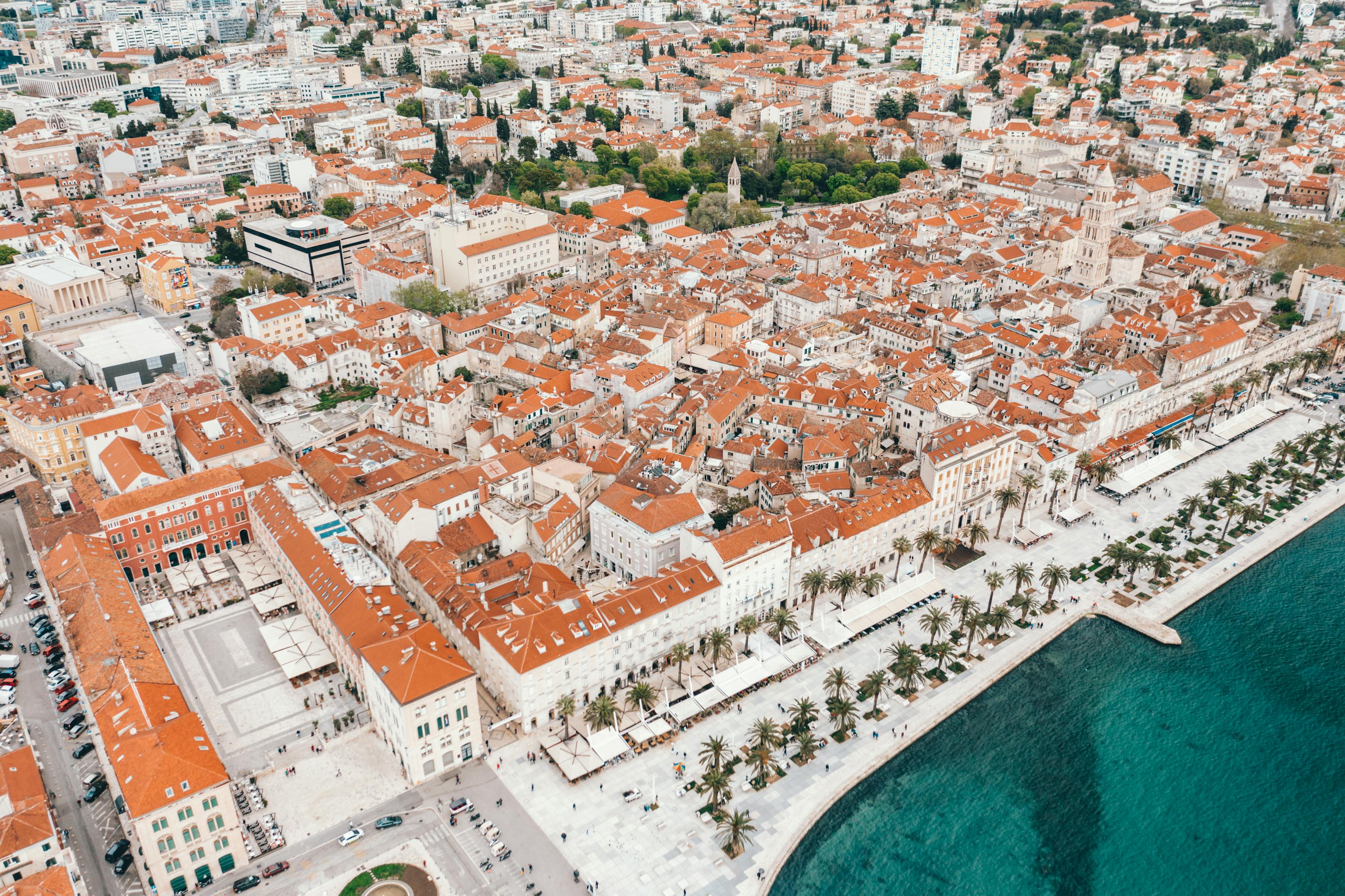 Amazing drone view of historical buildings with red tile roofs and modern promenade near turquoise sea in Split