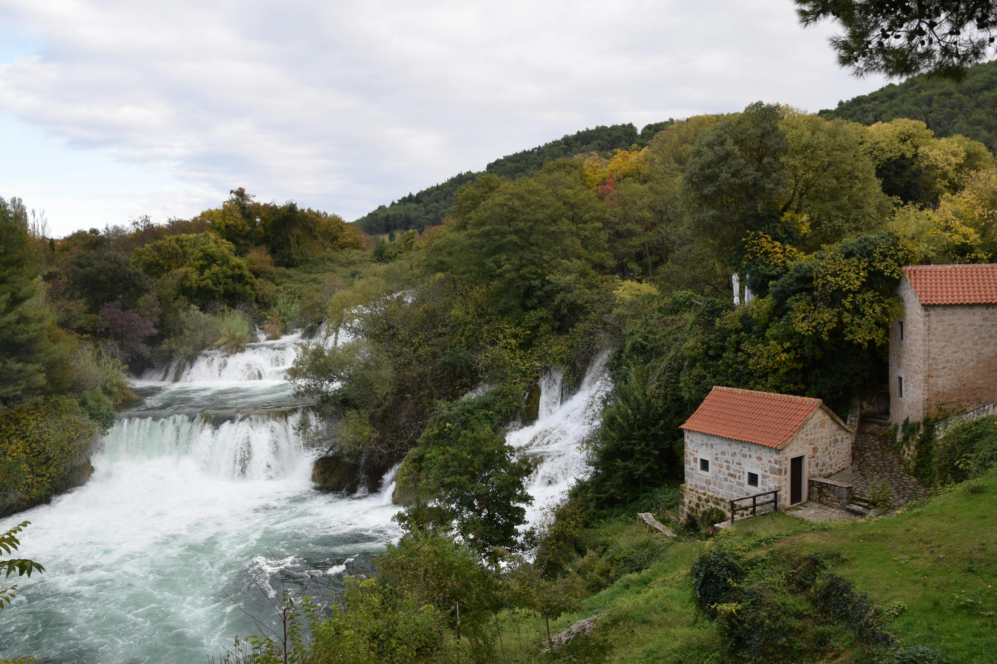 Picturesque view of waterfalls and a stone house amid lush greenery in Krka National Park