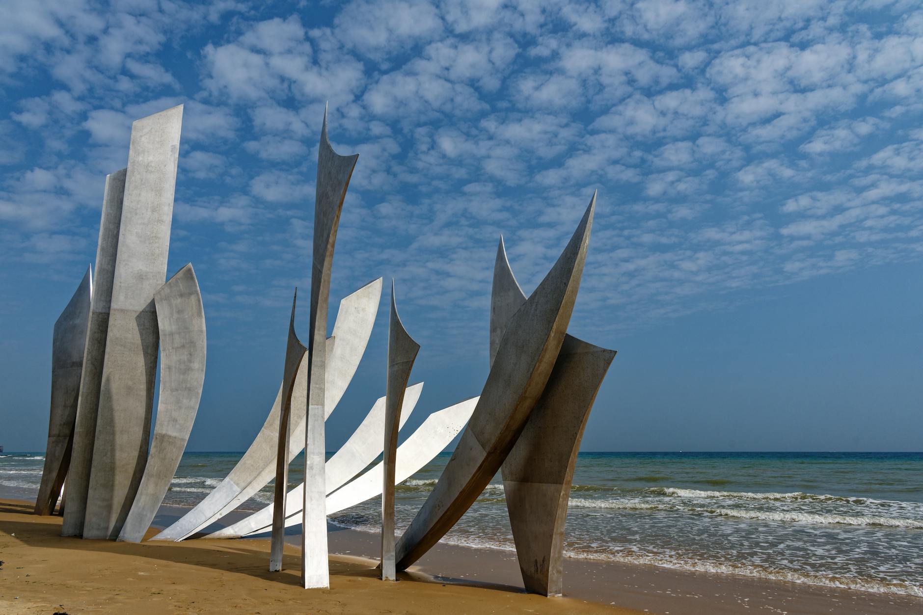 Wide view of Les Braves sculpture on Omaha Beach with beachgoers in the distance
