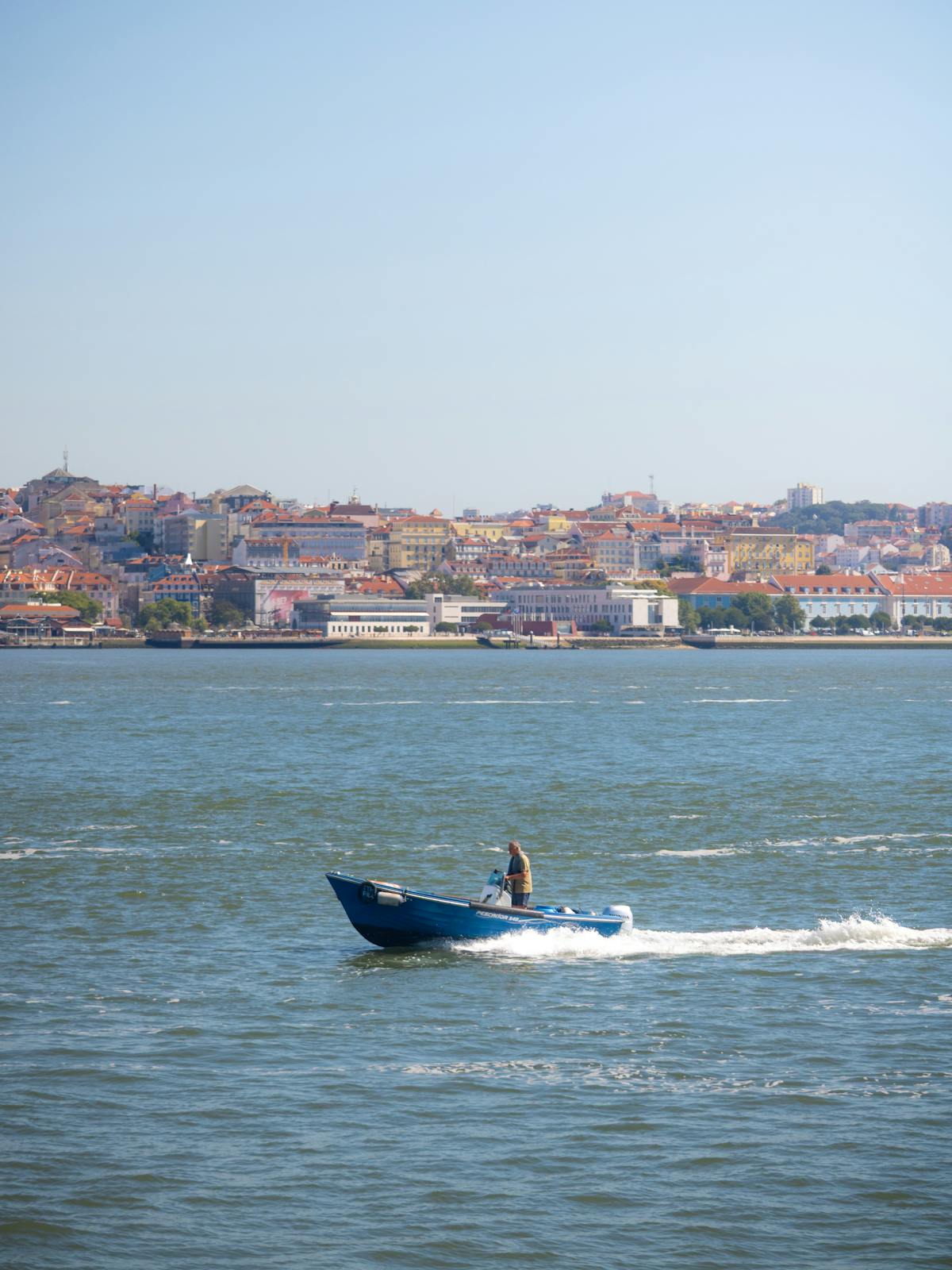 Small blue boat on the Tagus River with Lisbon cityscape behind
