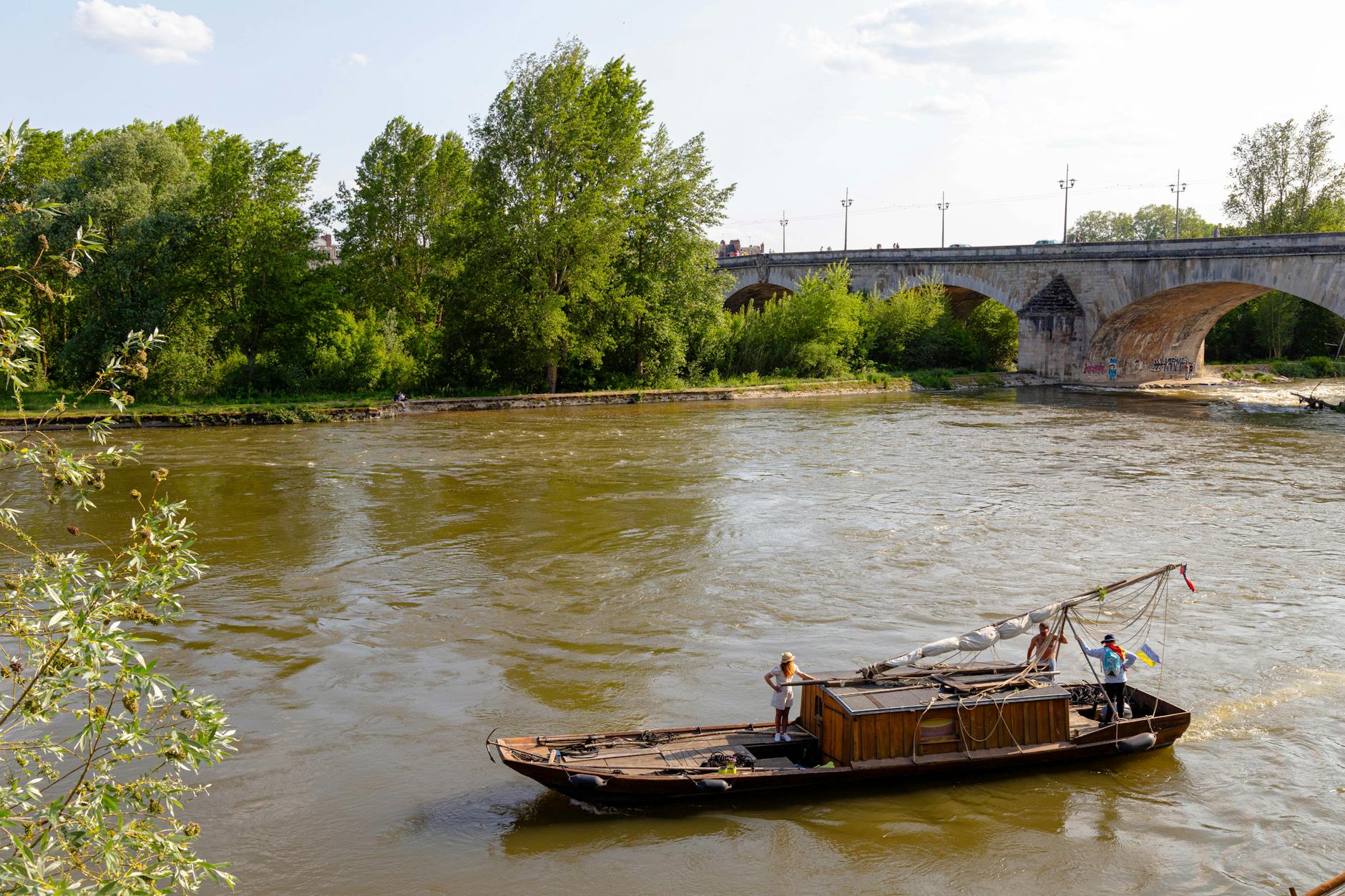 Traditional wooden boat sails along the Loire River under a historic stone bridge