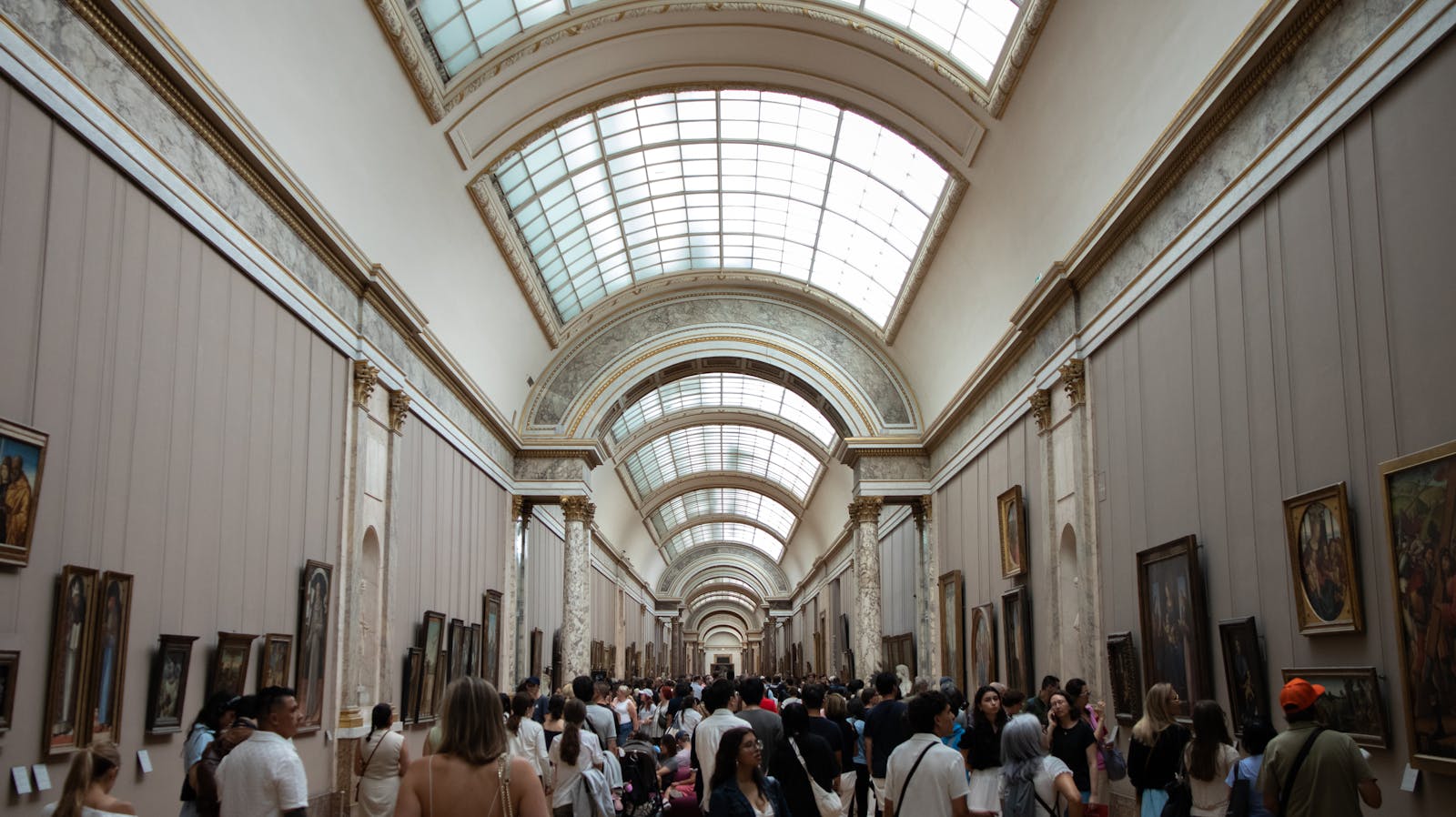 Visitors exploring a busy corridor with art exhibits at the Louvre Museum
