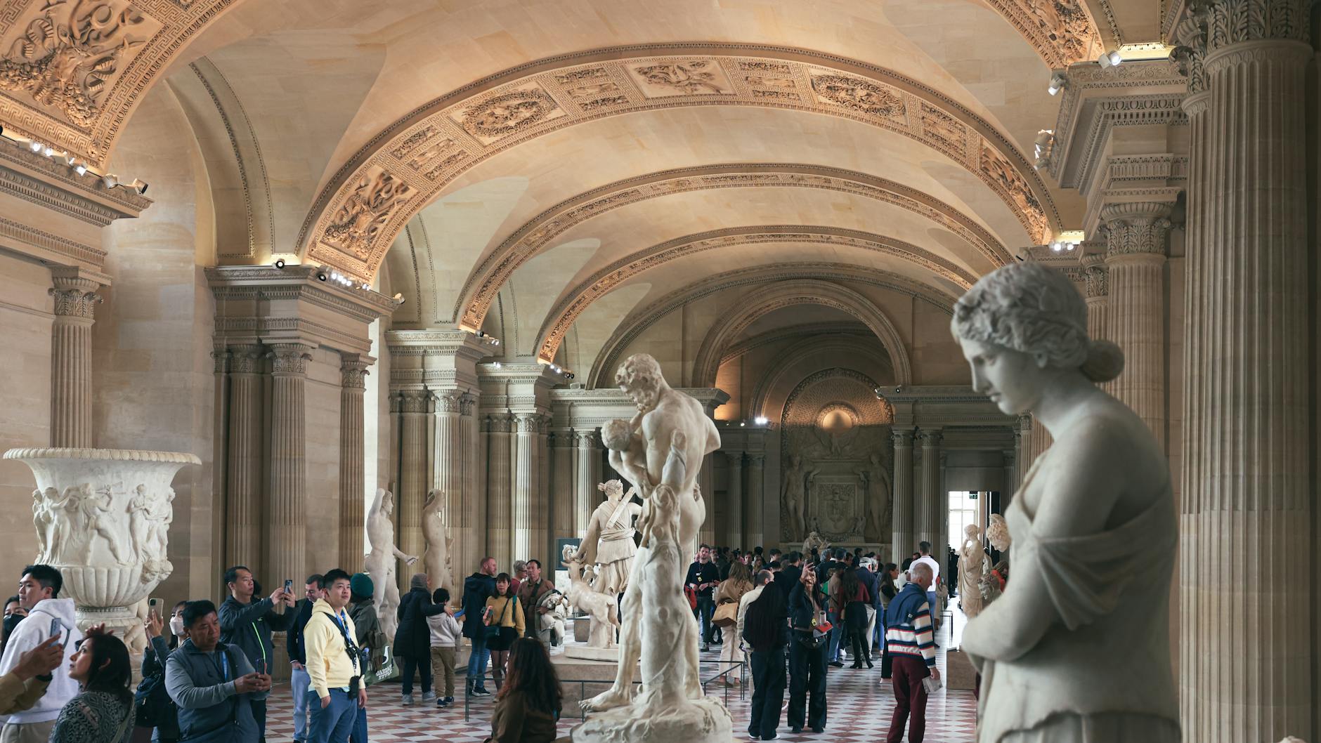 A crowded hall at the Louvre with classical statues and architecture
