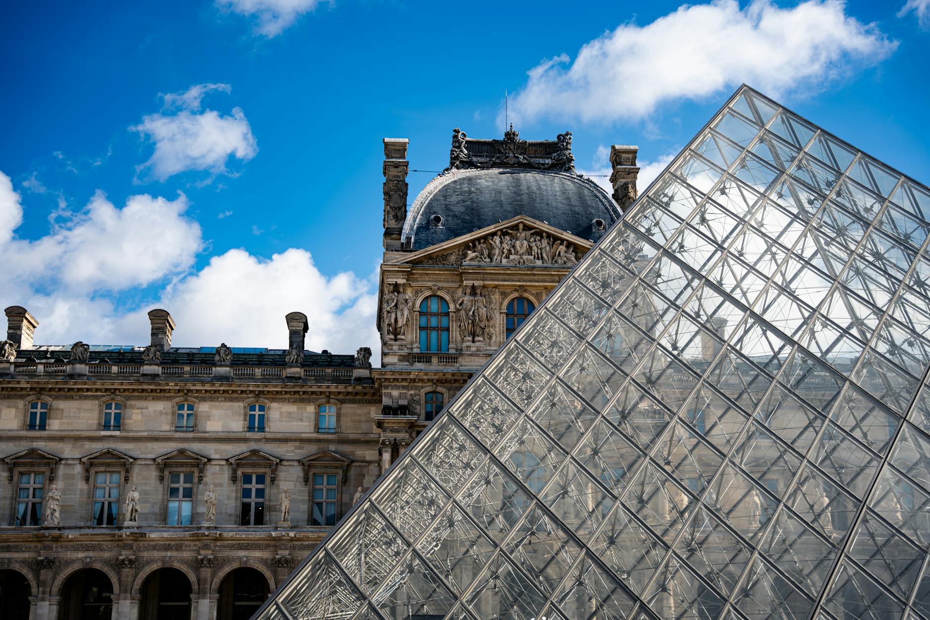 The Louvre Pyramid with blue sky and the historic museum building