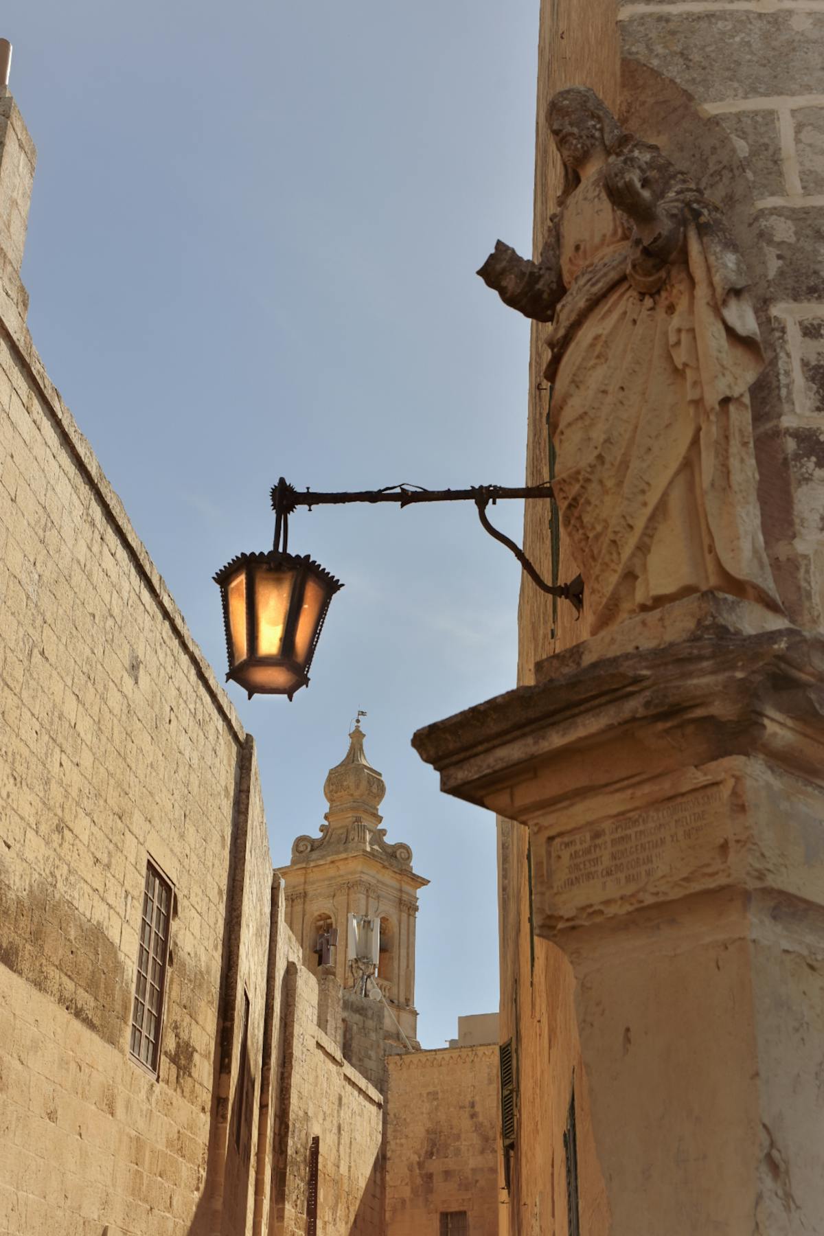 Historic street in Mdina with a traditional lantern and decorative sculpture