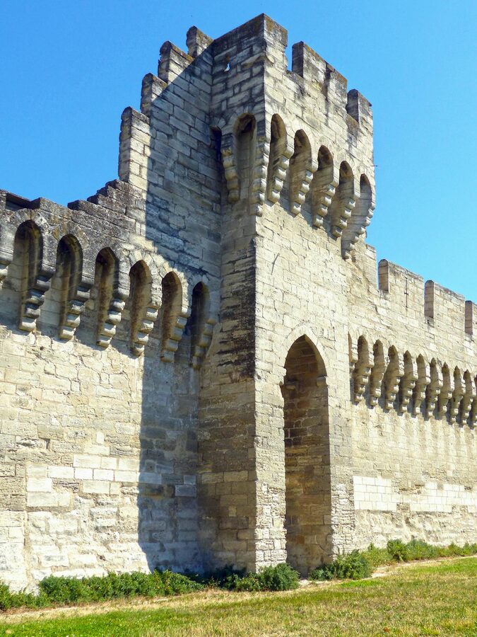 Medieval stone fortress wall in Avignon with crenellations under blue sky