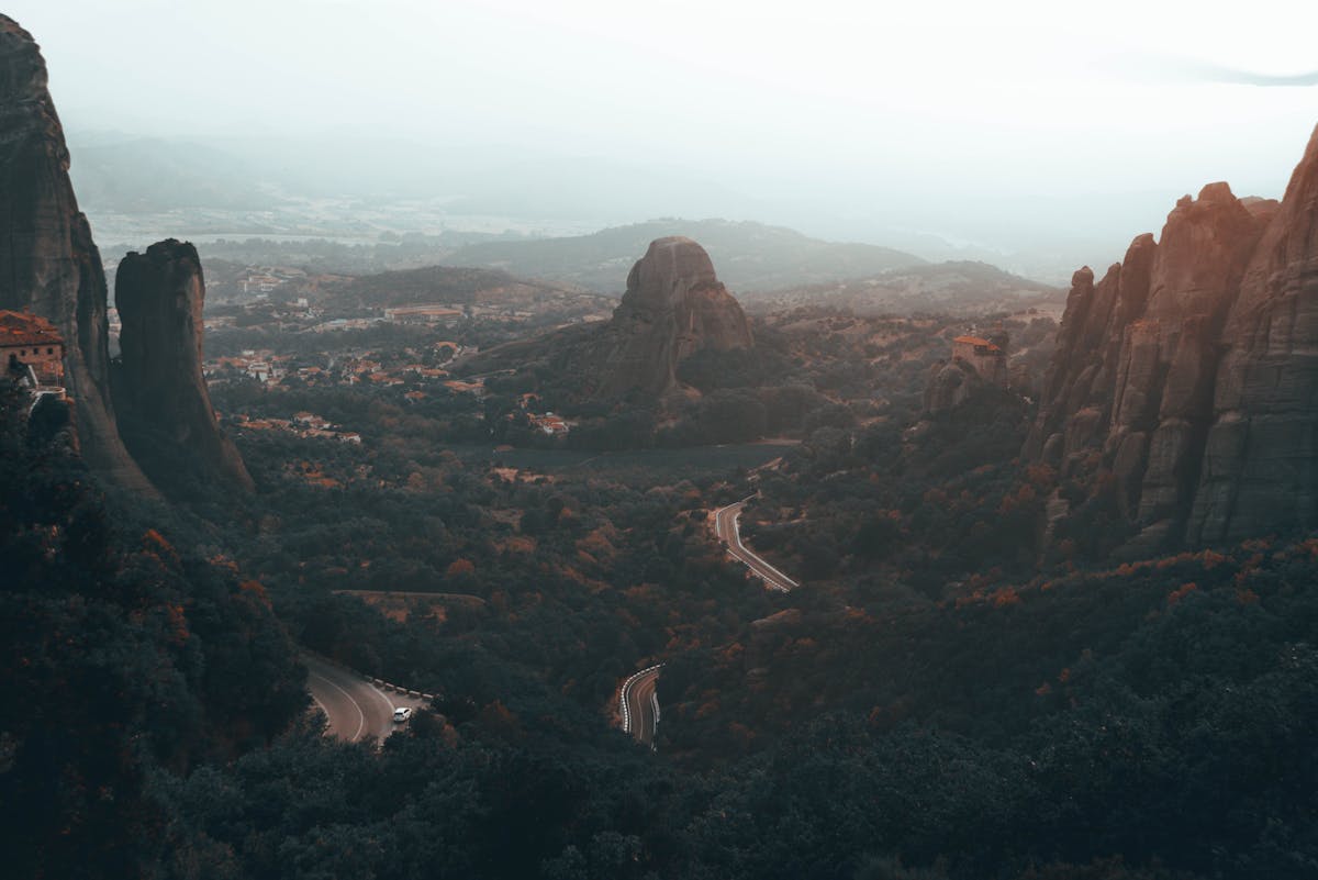 Aerial view of Meteora rock formations with winding roads and misty landscapes