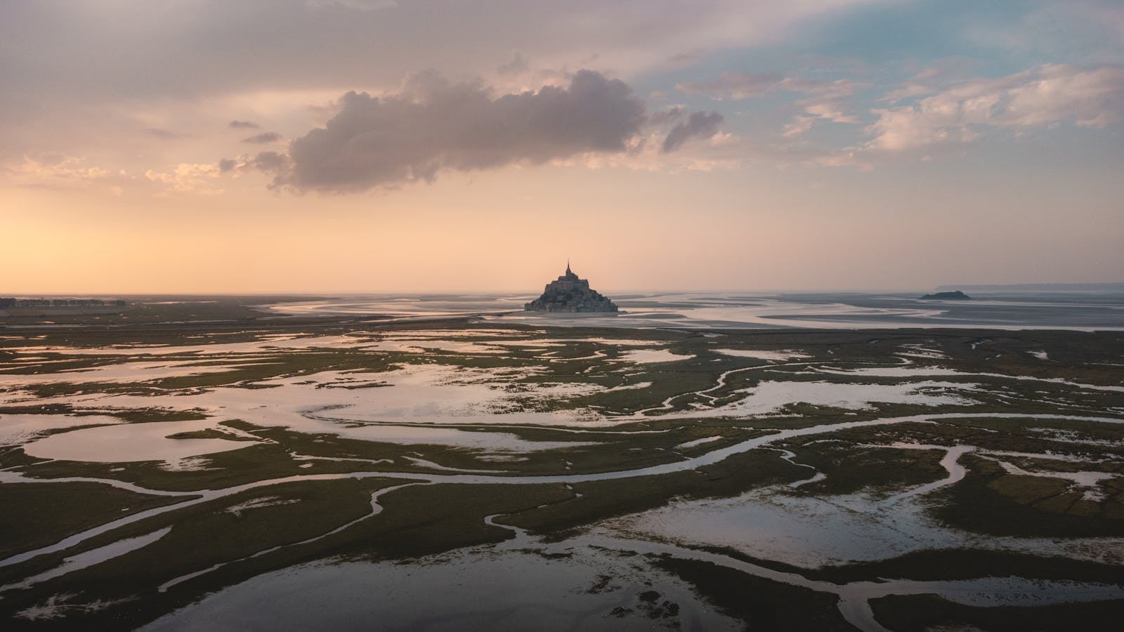 Aerial view of Mont Saint-Michel at low tide during sunset with reflective marshlands