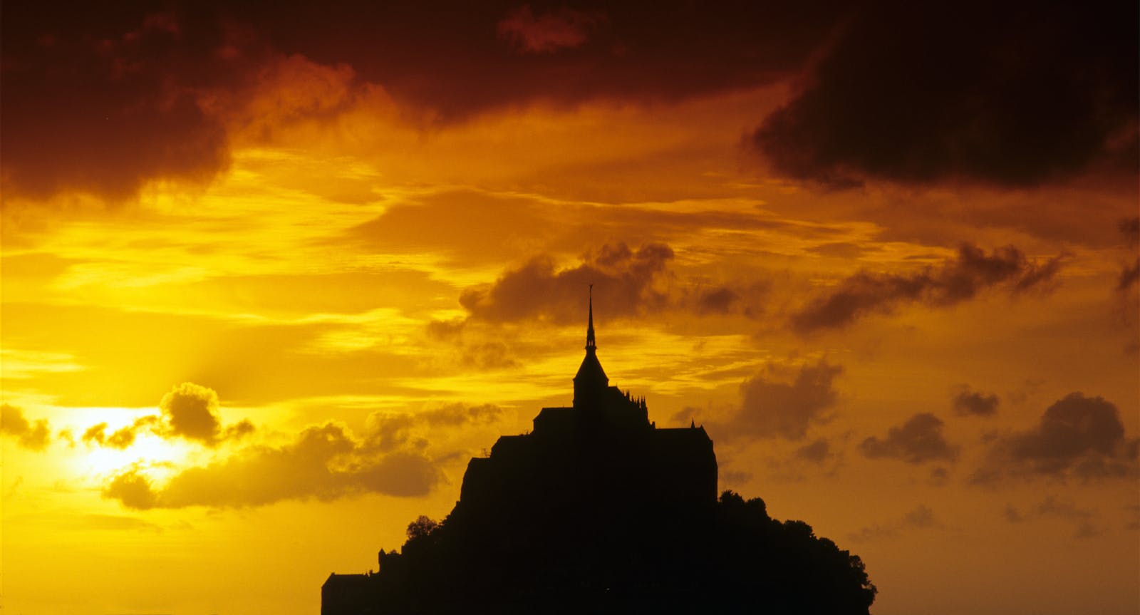 Silhouette of Mont Saint-Michel against a deep orange sunset sky