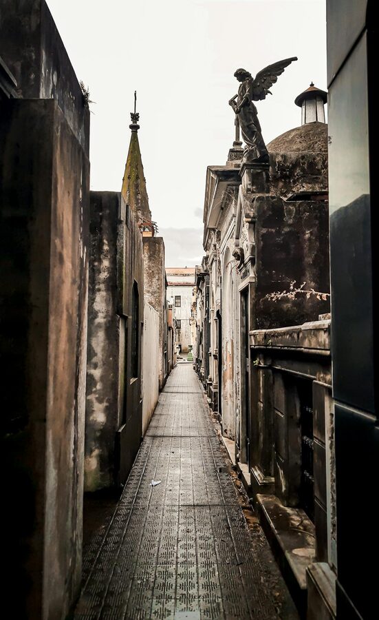 Narrow pathway in a historic cemetery with an angel statue and aged tombs