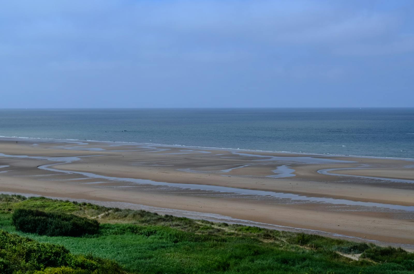The vast sand and calm sea of Omaha Beach in Normandy under clear blue skies