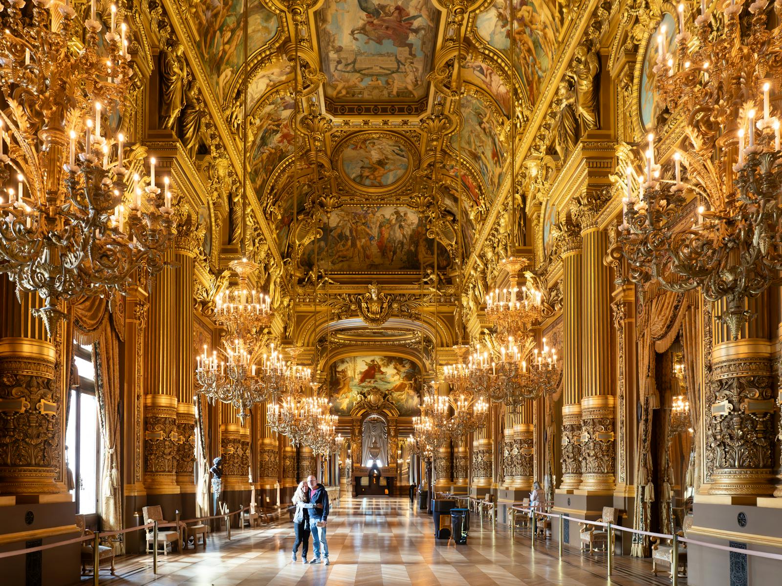 Opulent gold interior of Palais Garnier with chandeliers reflecting on mirrored walls