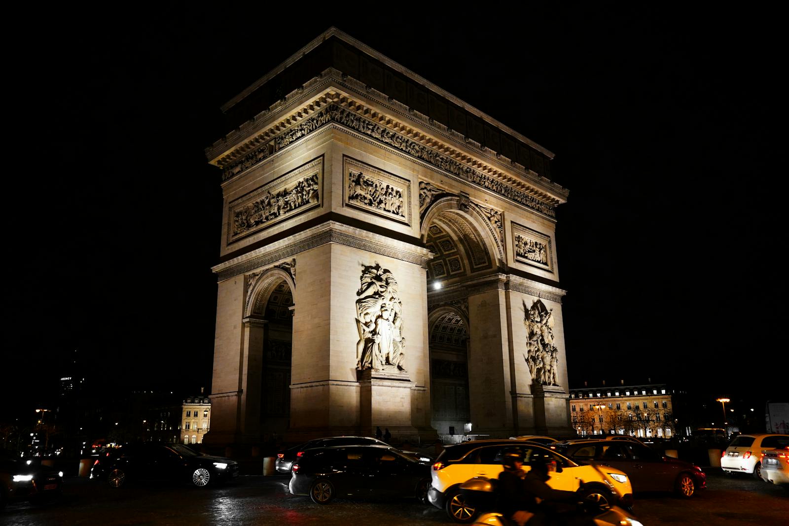 Illuminated Arc de Triomphe at night with Paris traffic flowing past