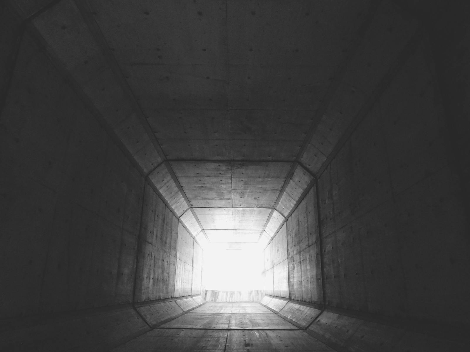 Long dim concrete tunnel with light at the end inside the Paris Catacombs