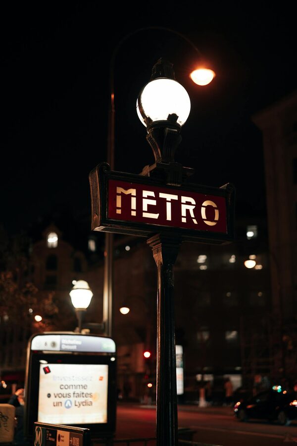 Illuminated Paris metro sign with vintage street lamps at night