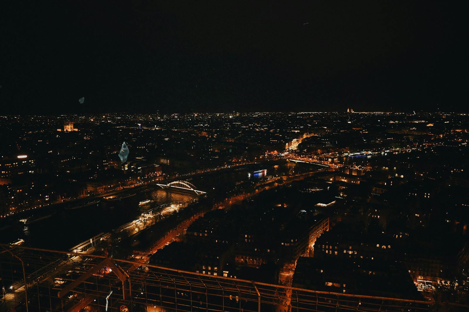Night view from the Eiffel Tower summit showing illuminated bridges and streets of Paris