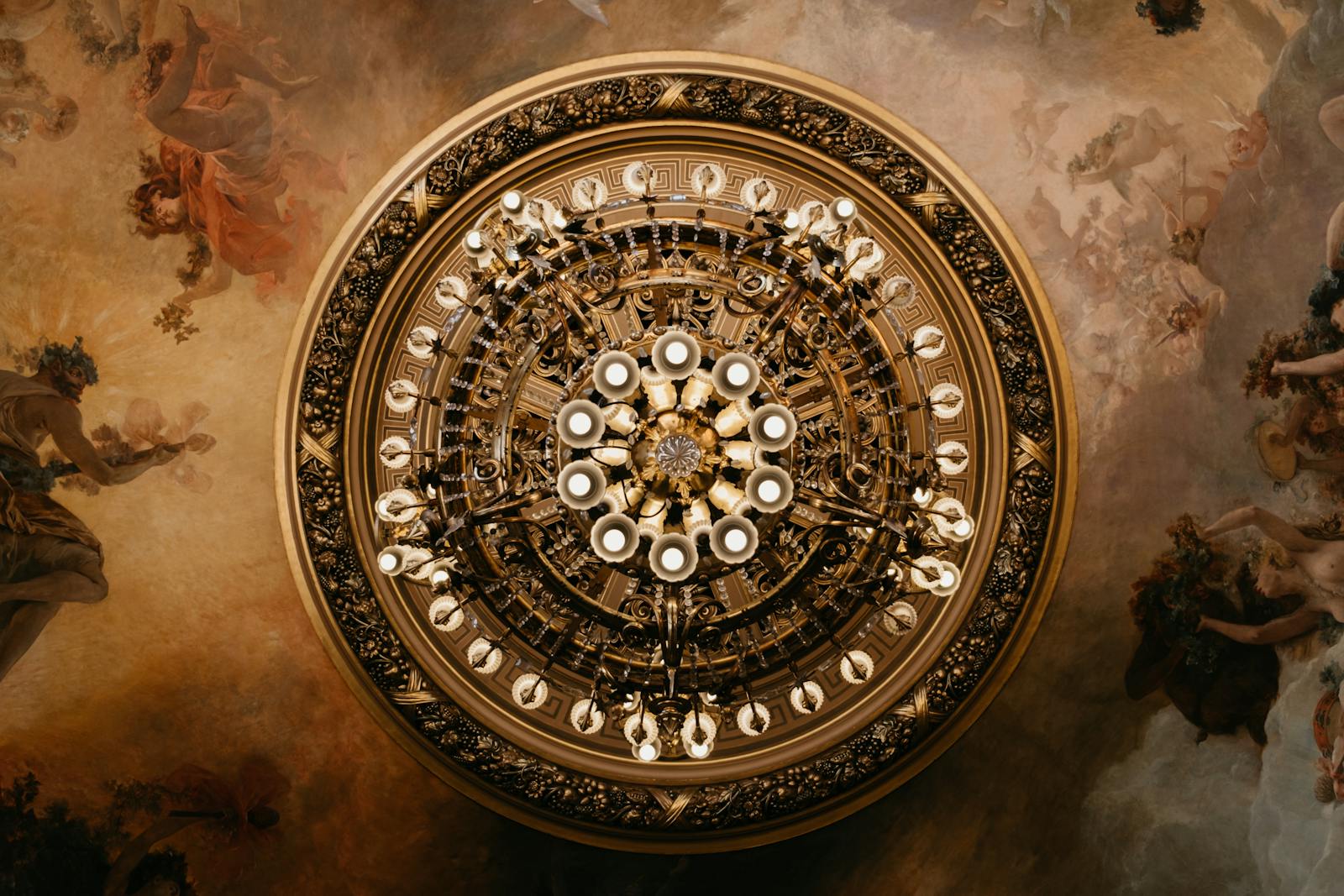 Intricate chandelier glowing below the decorated ceiling of the Paris opera house