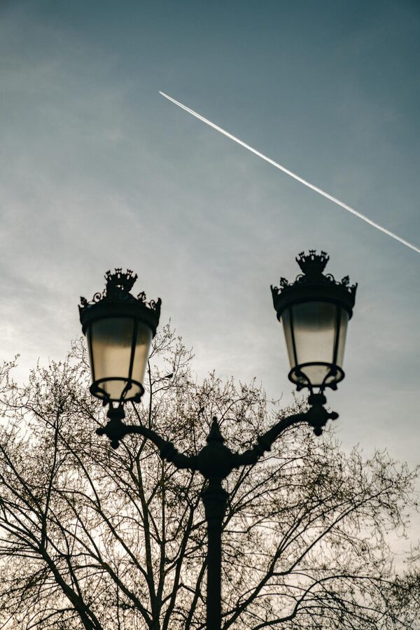 Silhouetted street lamps in Paris at twilight with contrail-streaked sky