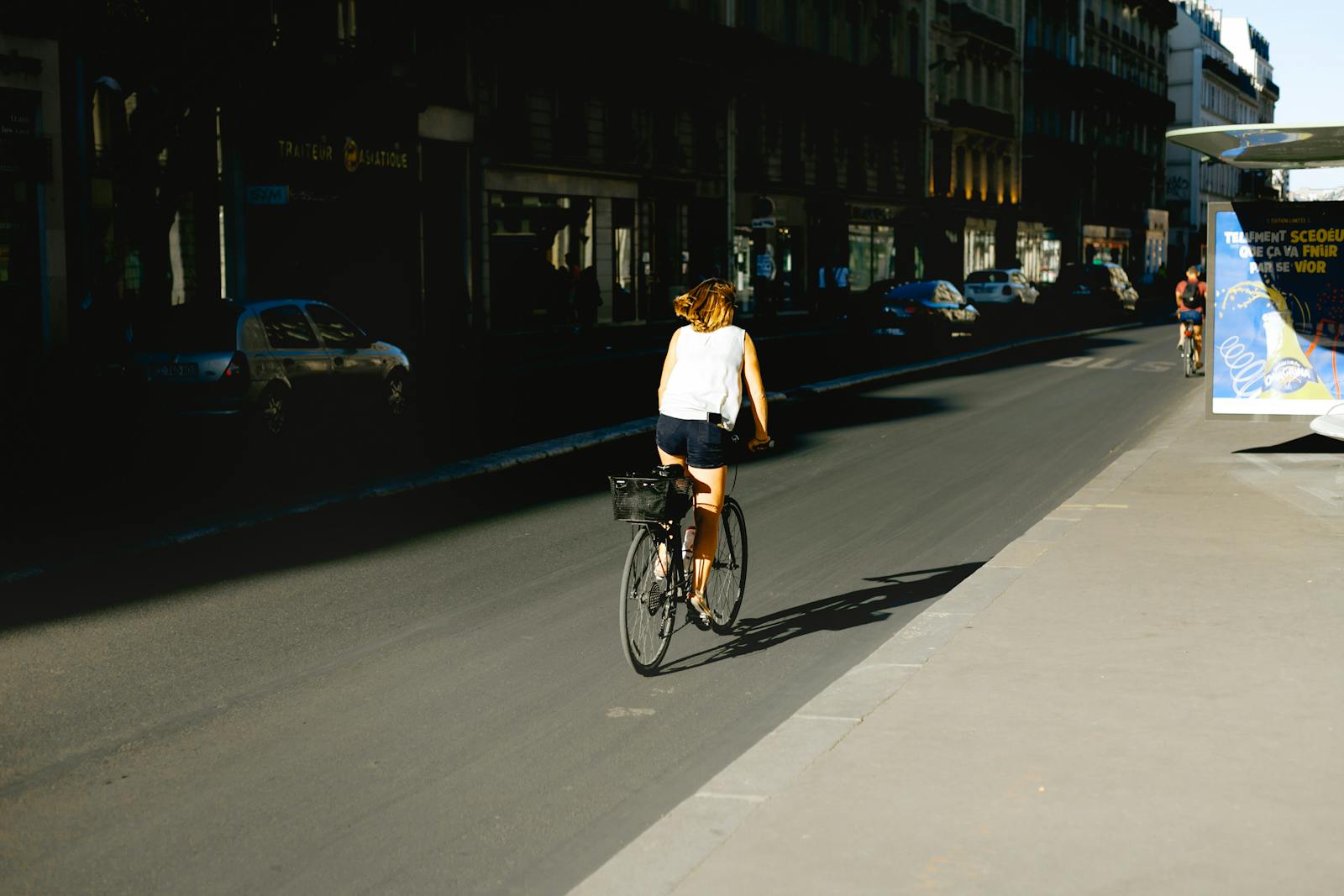 A woman cycles through a sunlit Paris street showcasing urban life