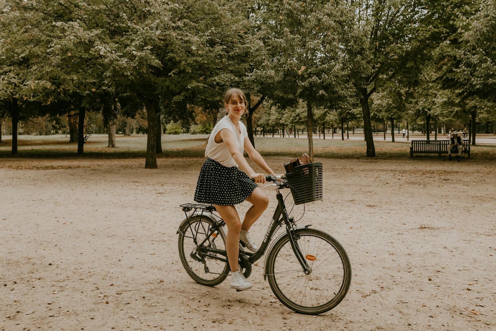 A young woman riding her bicycle along a tree-lined path in a Parisian park