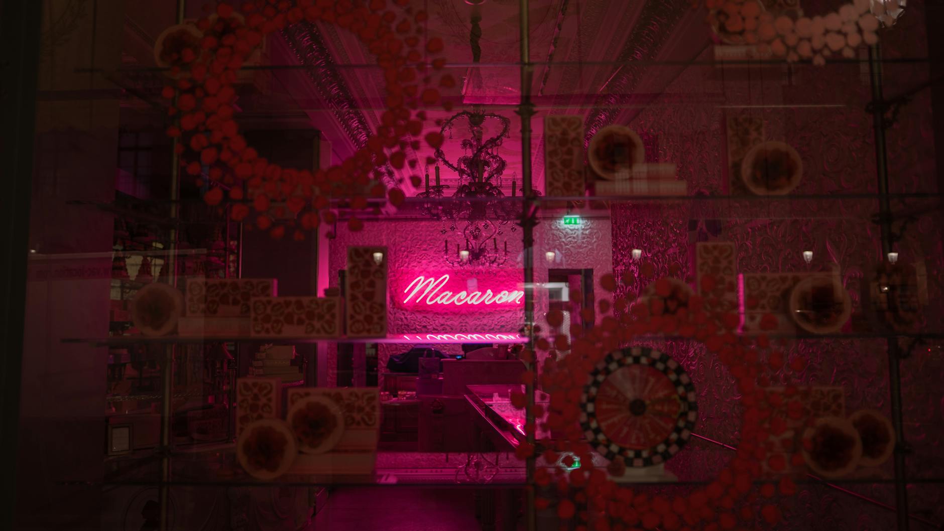 Neon-lit Parisian bakery showcasing macaron display through glass shelves