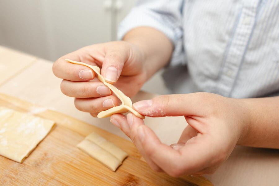 Hands shaping fresh pasta dough on a wooden board
