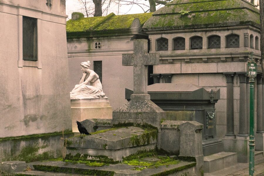 Statues and a crow in Pere Lachaise Cemetery Paris creating an eerie atmosphere