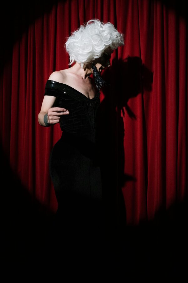 Performer in black dress on stage with red curtain
