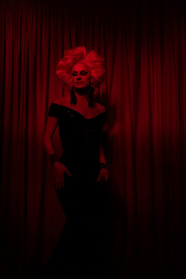 Performer in glamorous black dress against a red curtain backdrop