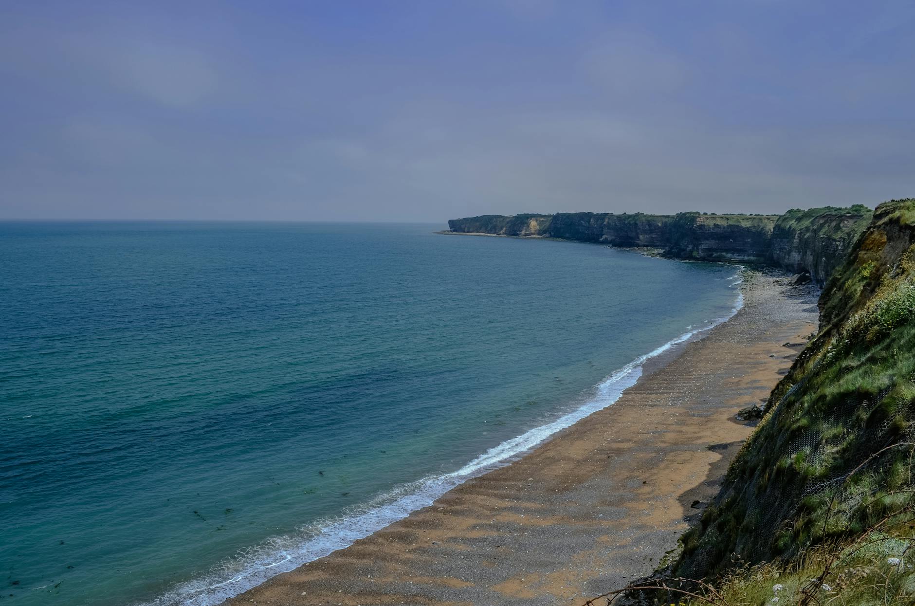 Rugged limestone cliffs and beach at Pointe du Hoc Normandy under clear sky