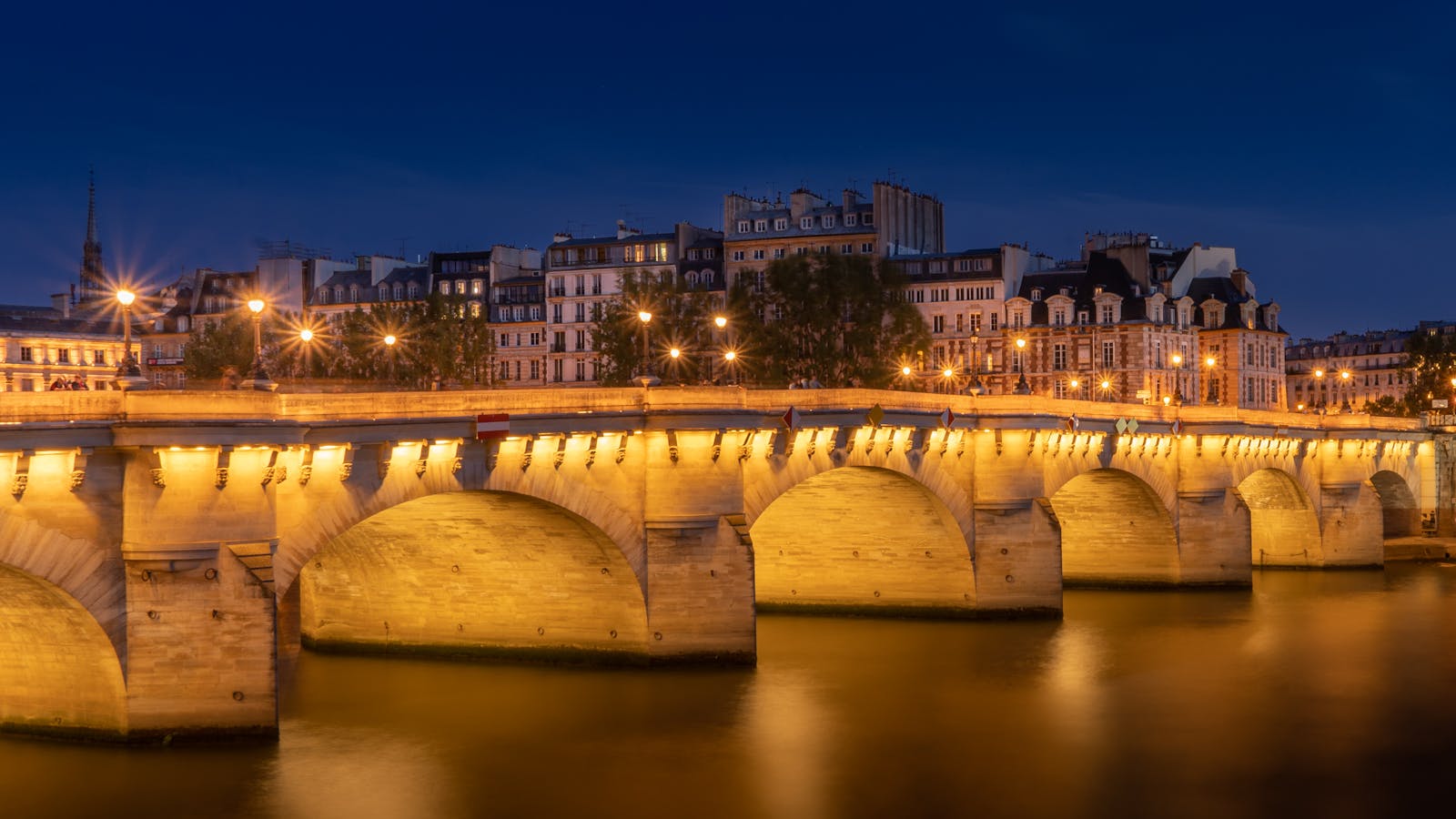 Pont Neuf bridge illuminated at night reflecting on the Seine River