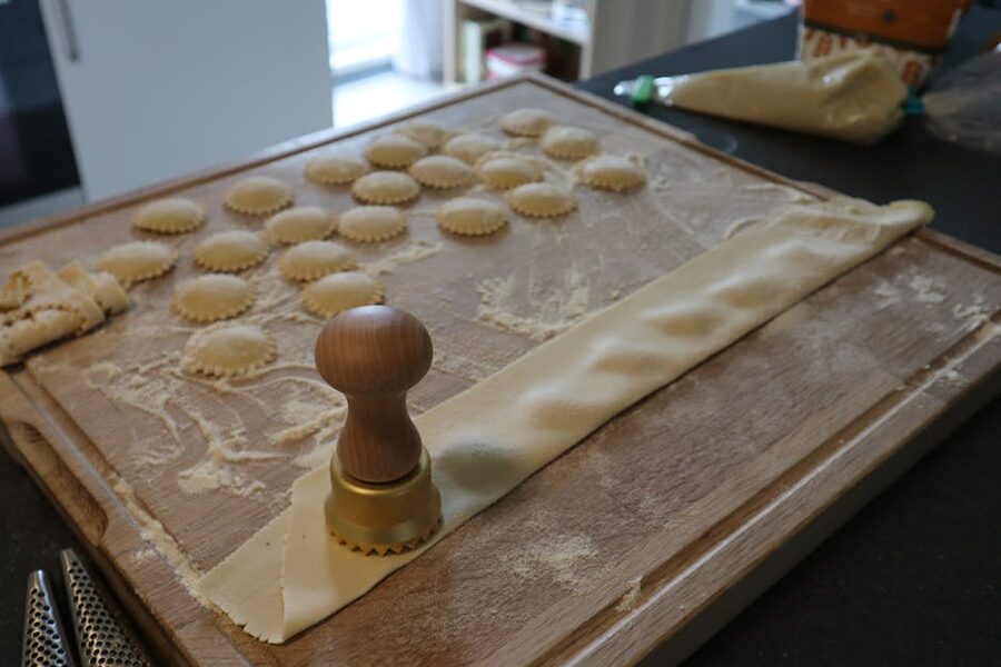 Wooden dough cutter and ravioli on floured board