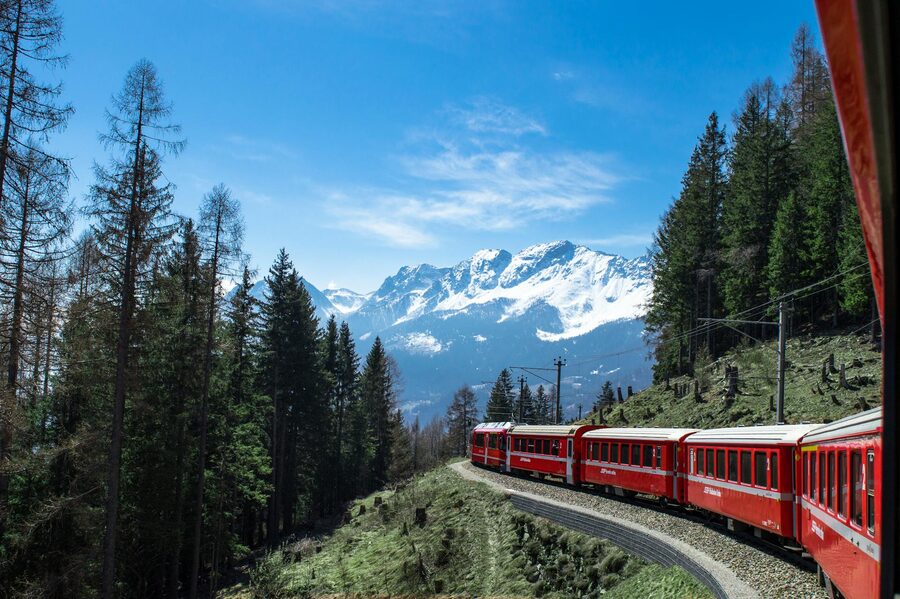 Red train travelling through forests and snowy mountains