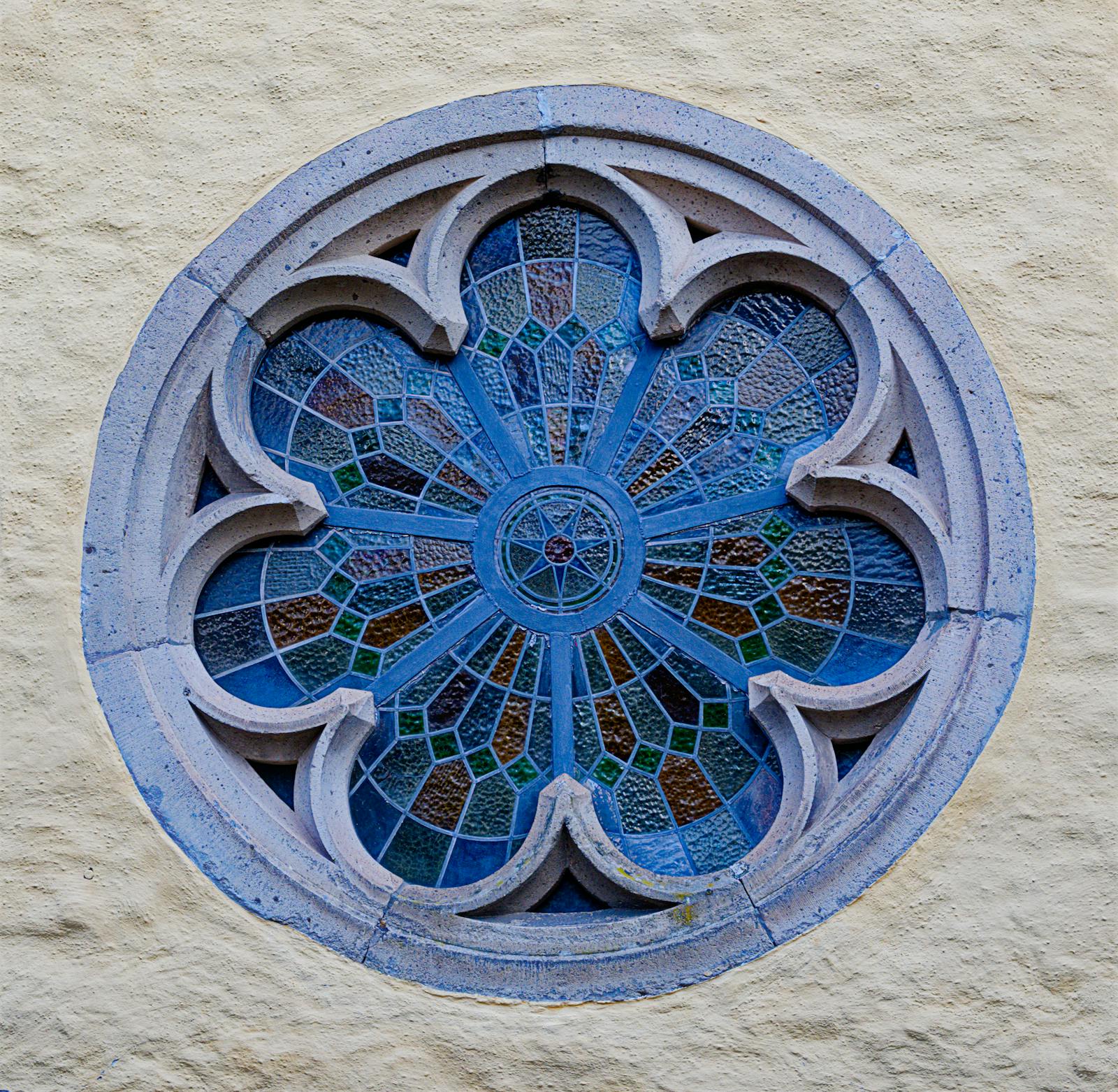 Round stained-glass window with floral patterns inside a gothic cathedral