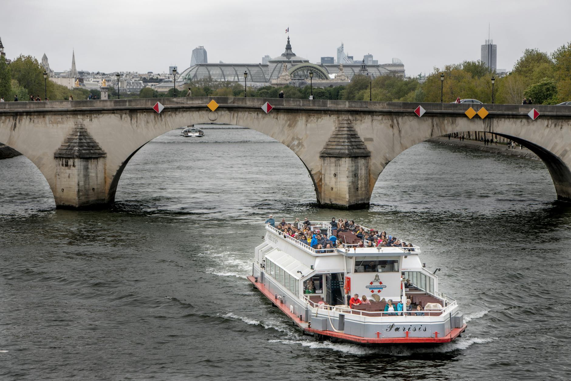A sightseeing cruise boat passing under an iconic Seine river bridge in Paris