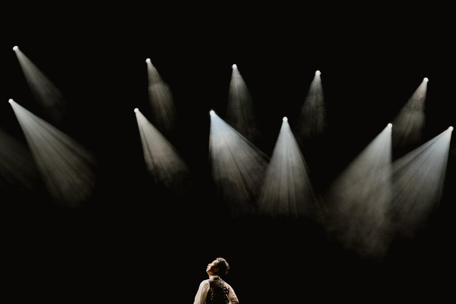 Solo performer standing in a spotlight on a dark stage