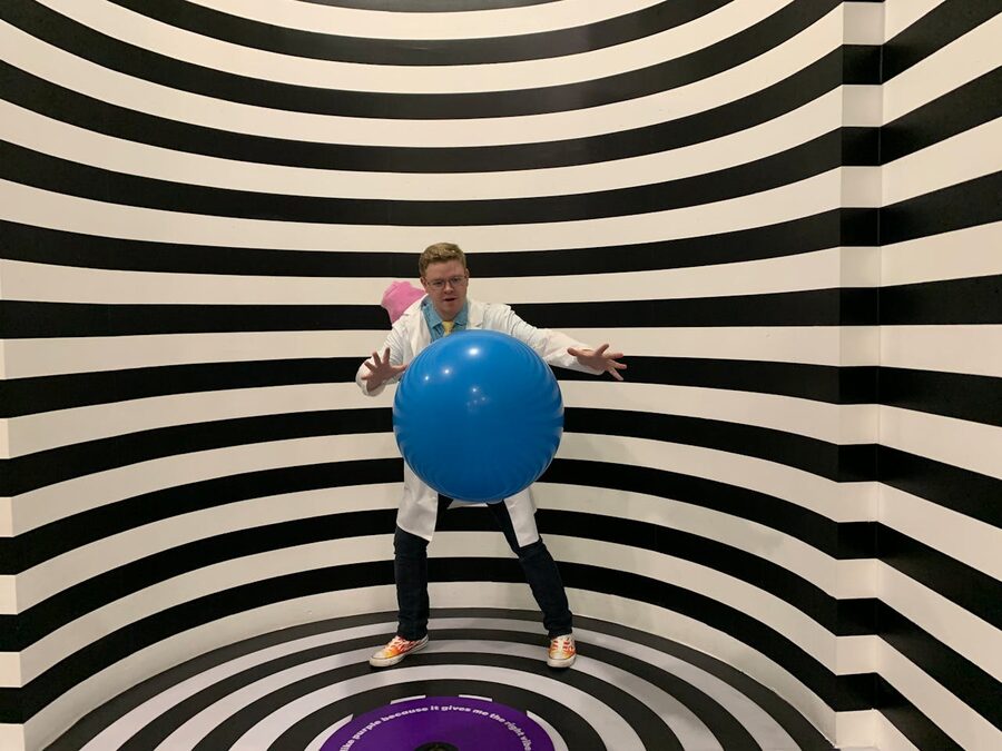 Man posing with a blue ball in a striped illusion room