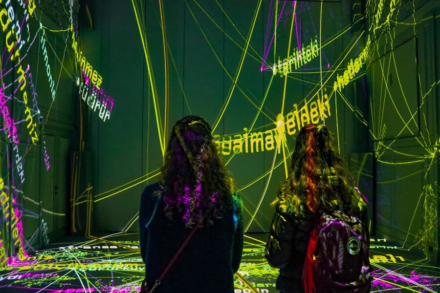 Two women observe a text projection art installation in a dark room