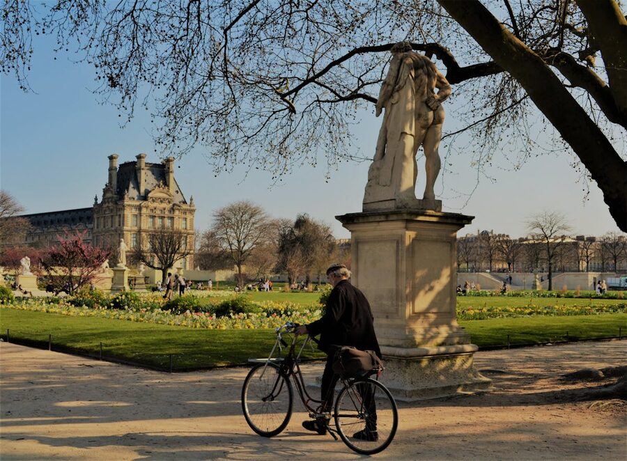 Cyclist passing a statue in Tuileries Garden with Louvre Palace backdrop