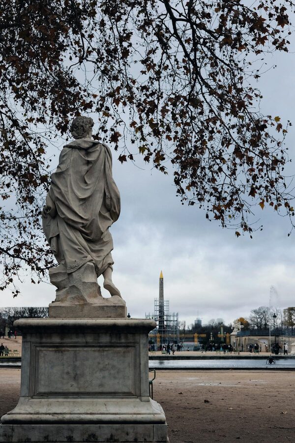 Marble statue in Tuileries Garden with Luxor Obelisk in Paris