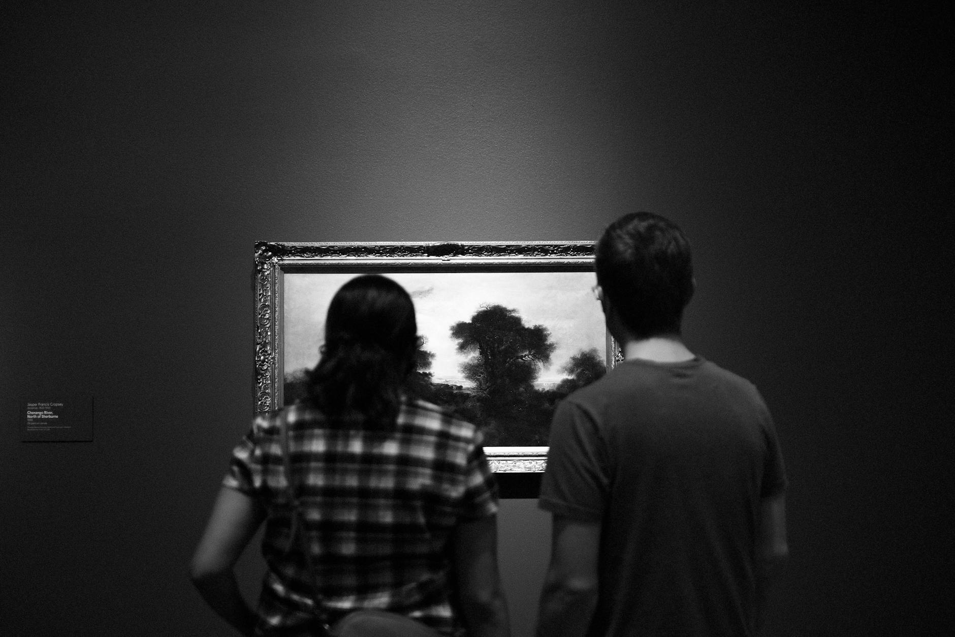 Two people viewing a painting in an art museum, shown in black and white