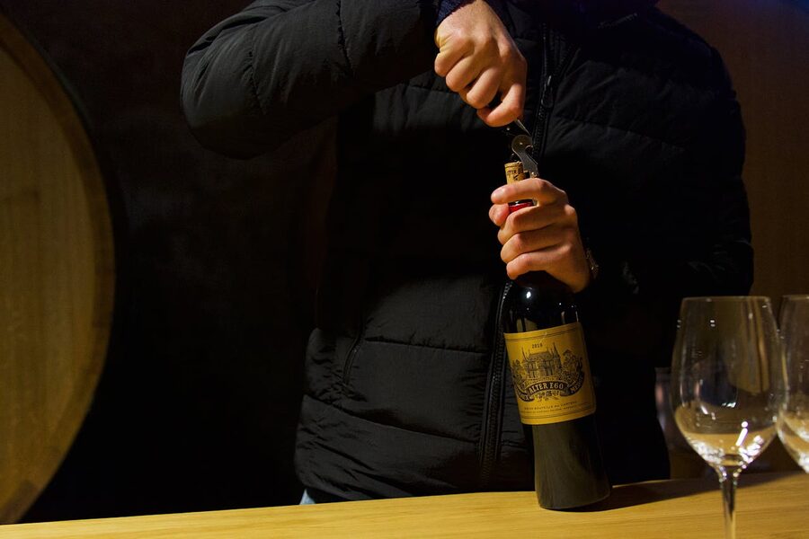 Person uncorking a wine bottle in a Bordeaux wine cellar