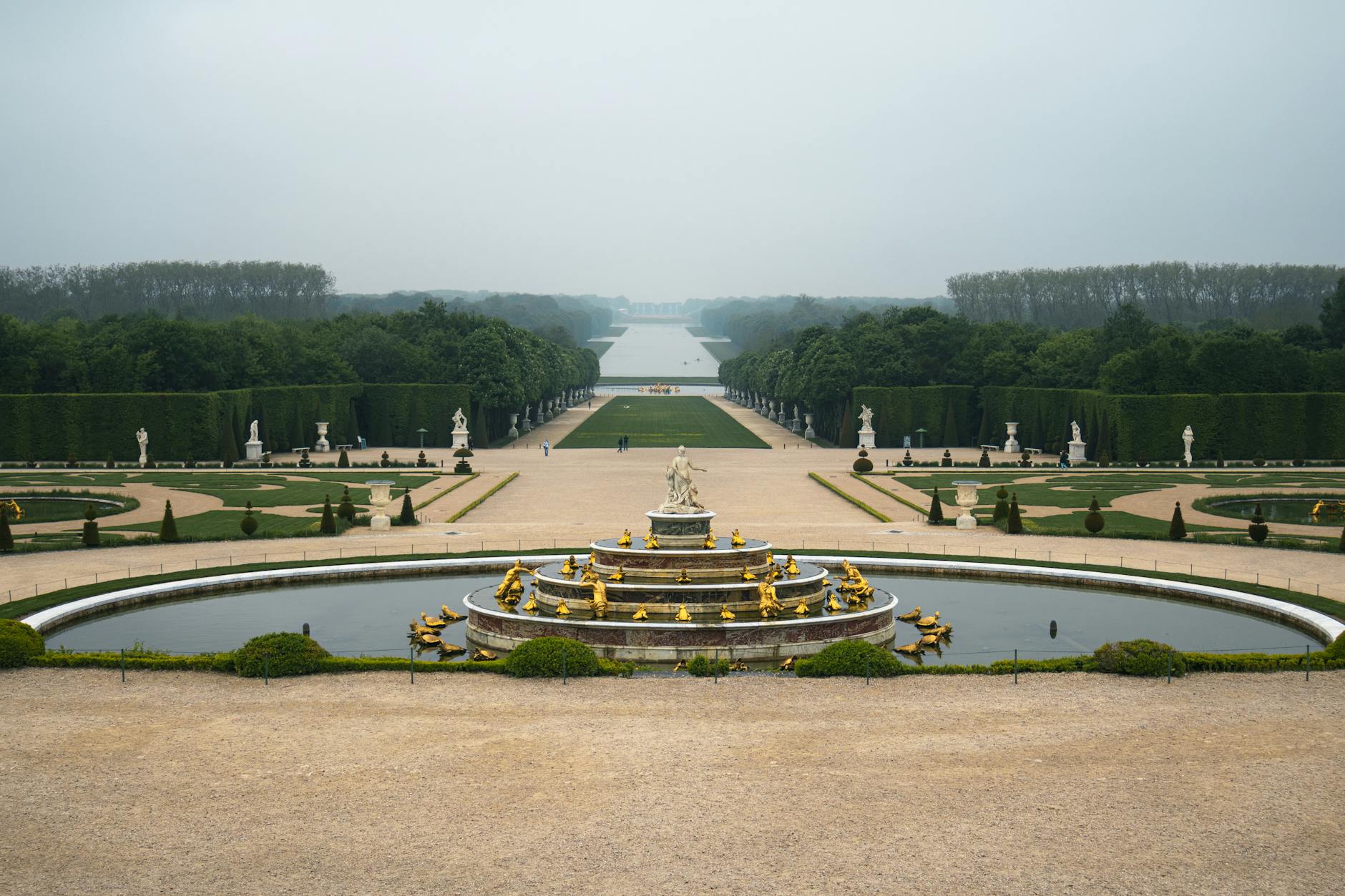 A fountain surrounded by the lush Versailles gardens in morning mist