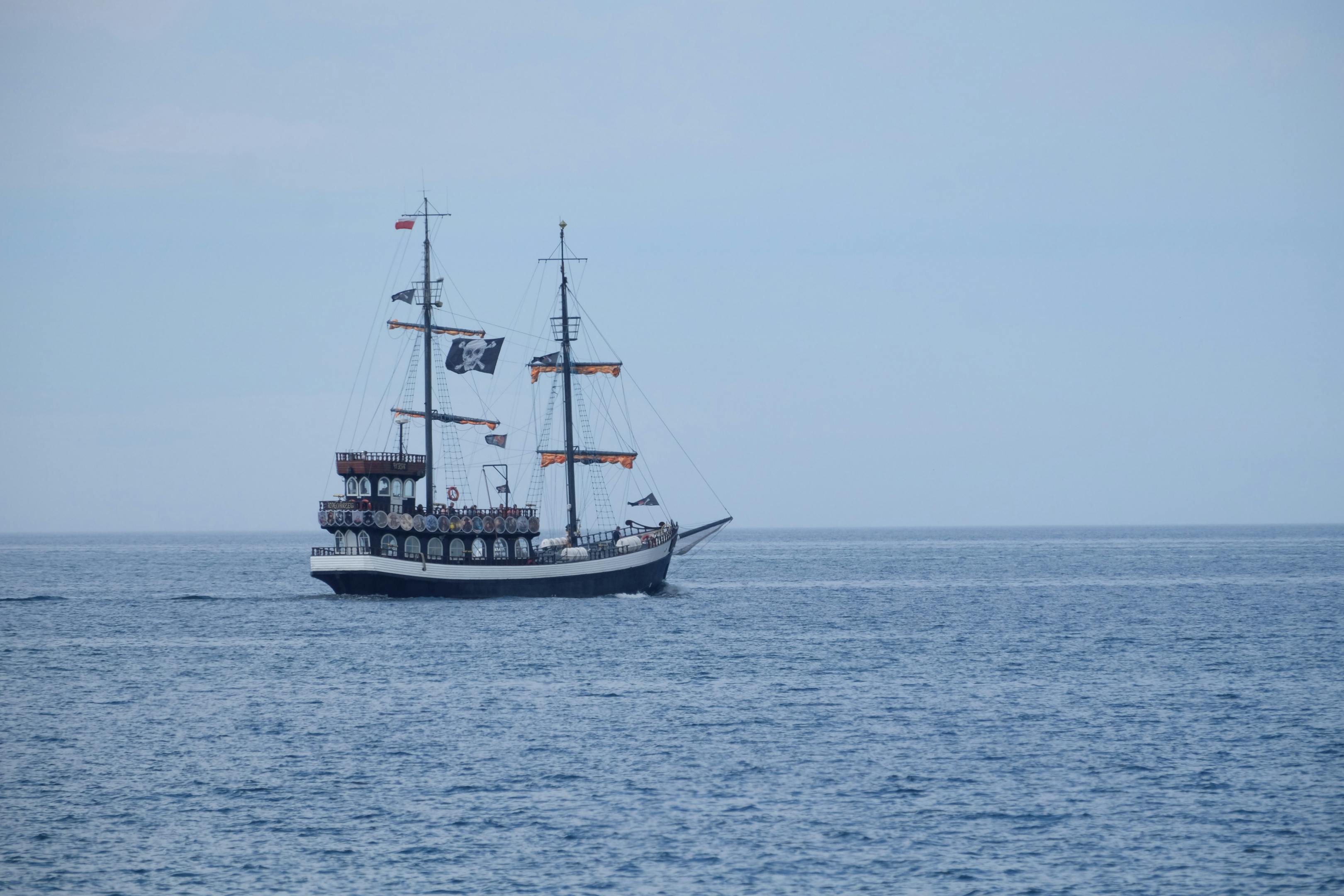 A vintage pirate ship with sails unfolds on calm ocean waters under a clear sky