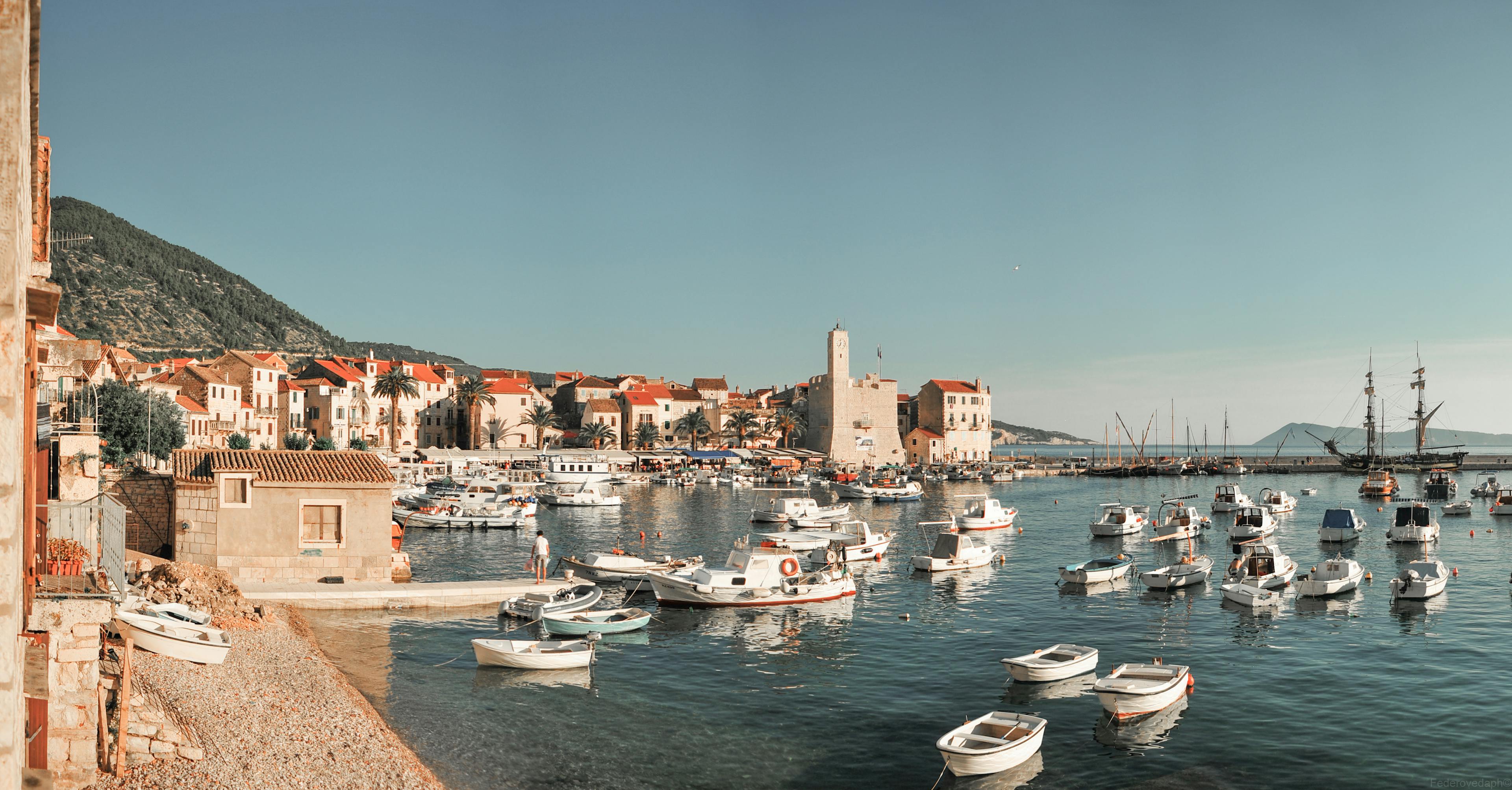 A picturesque view of Komiza harbor in Croatia with boats, historic buildings, and calm sea