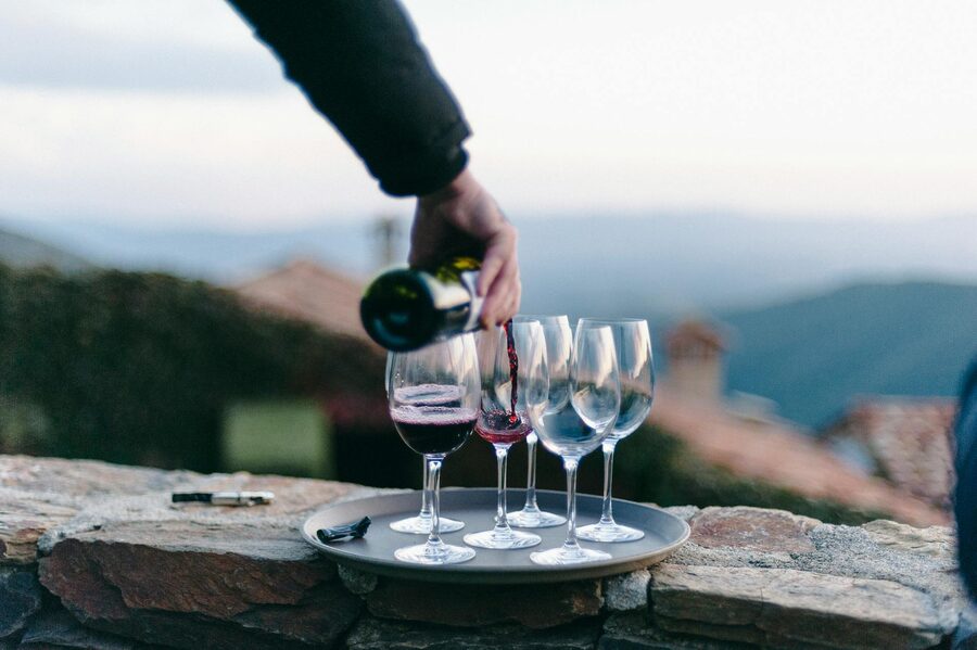 Hand pouring red wine into glasses with hills in the background