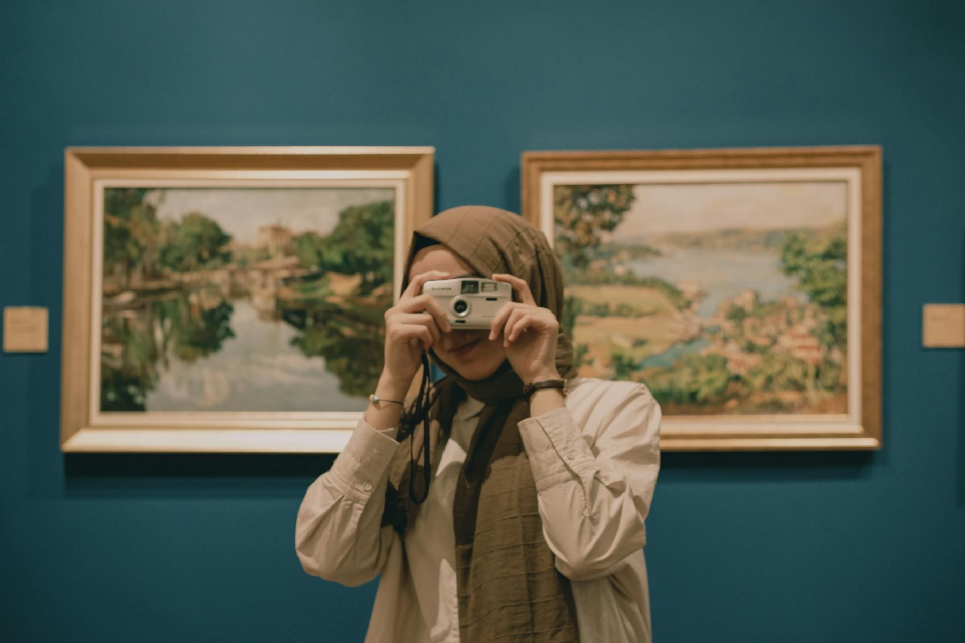 A woman capturing art and paintings in a gallery setting with her phone