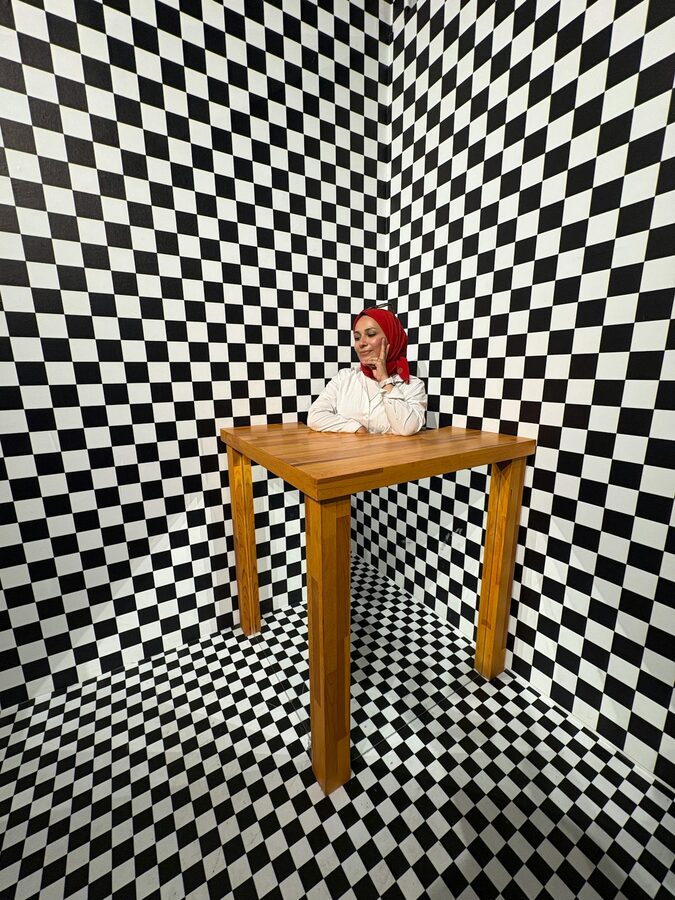 Woman sitting in a checkered pattern room creating an optical illusion
