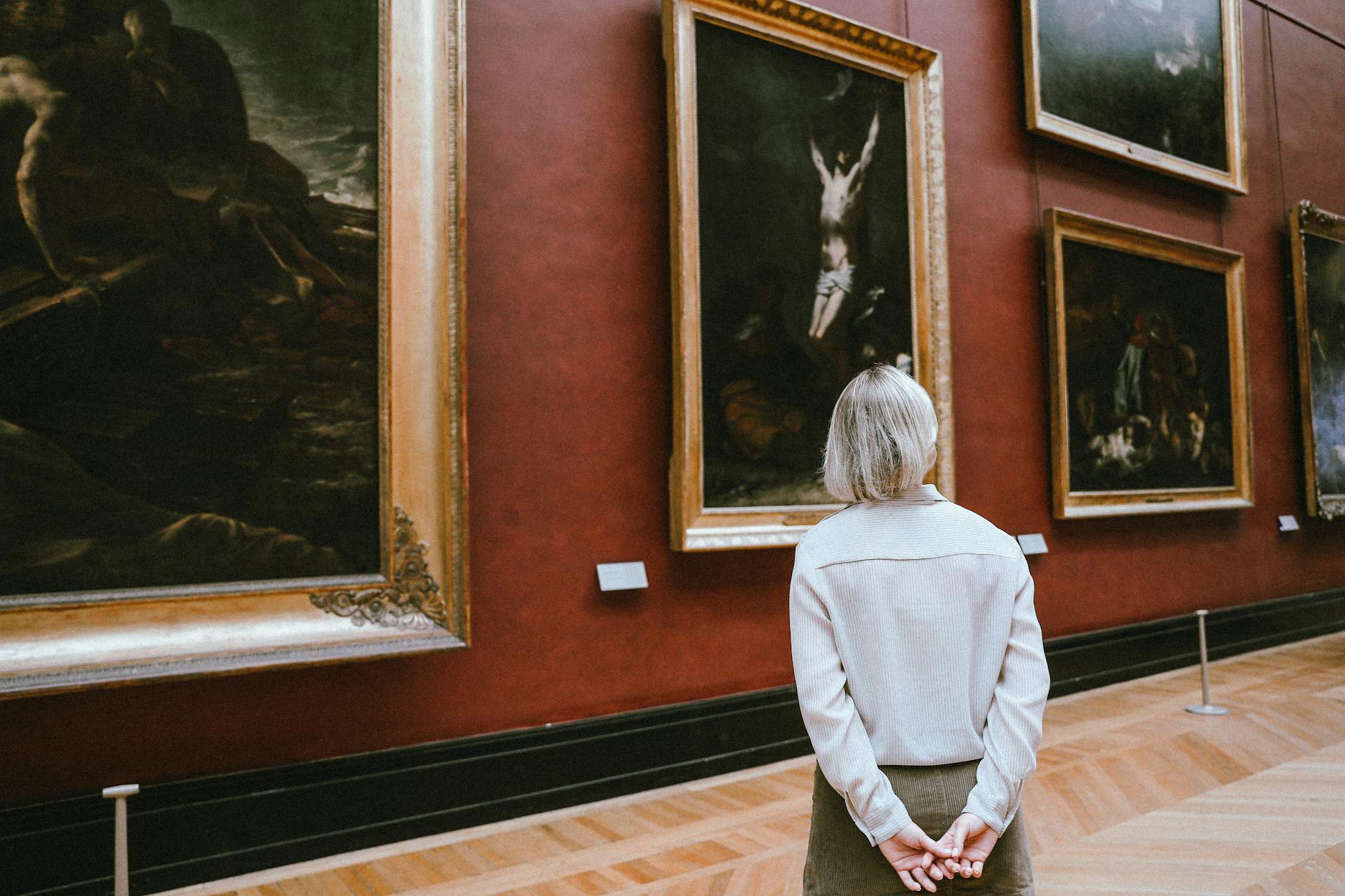 A woman observing paintings in a museum, shown from a back view
